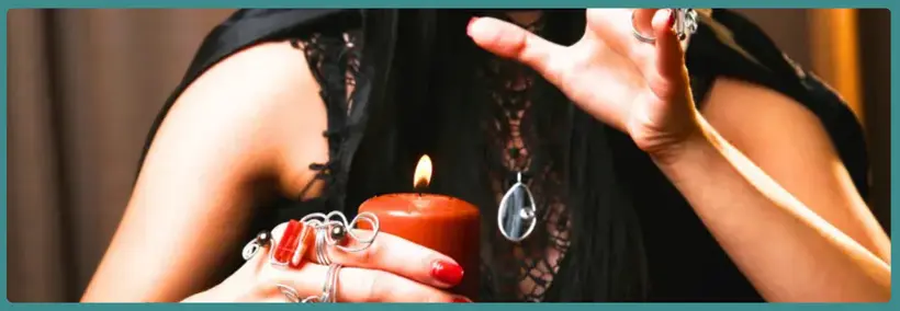 Hands holding a dark crystal or stone object above a lit red candle, creating an atmospheric mystical scene.